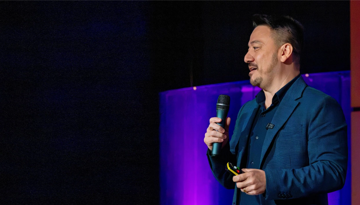 Vinicius Sasaki no palco, de microfone na mão, durante uma palestra
